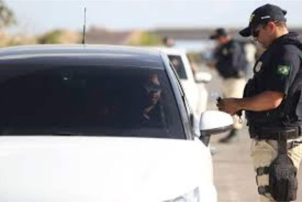 Policial aborda carro branco em operação de trânsito.