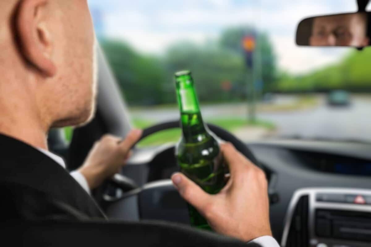 Pessoa dirigindo com garrafa de cerveja na mão.
