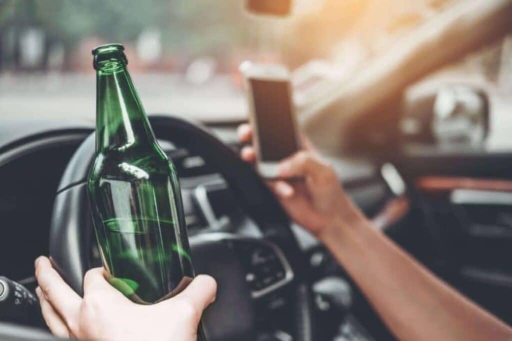 Motorista segurando garrafa de bebida e celular ao dirigir.
