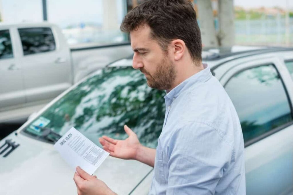 Homem confuso segurando papel perto do carro.