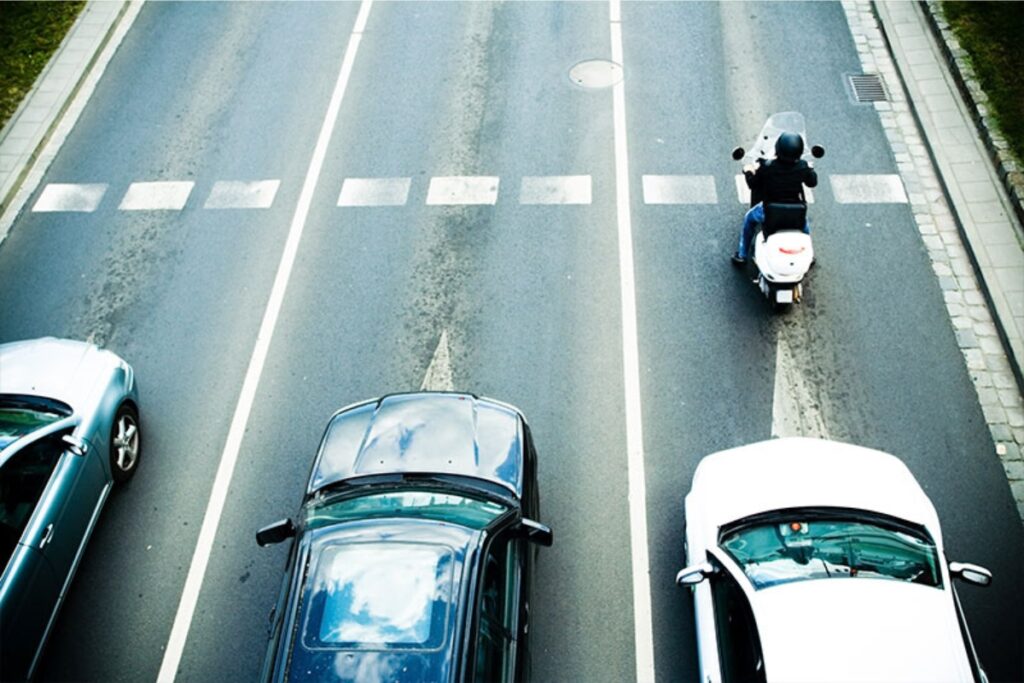 Trânsito com carros e moto na faixa de pedestres.